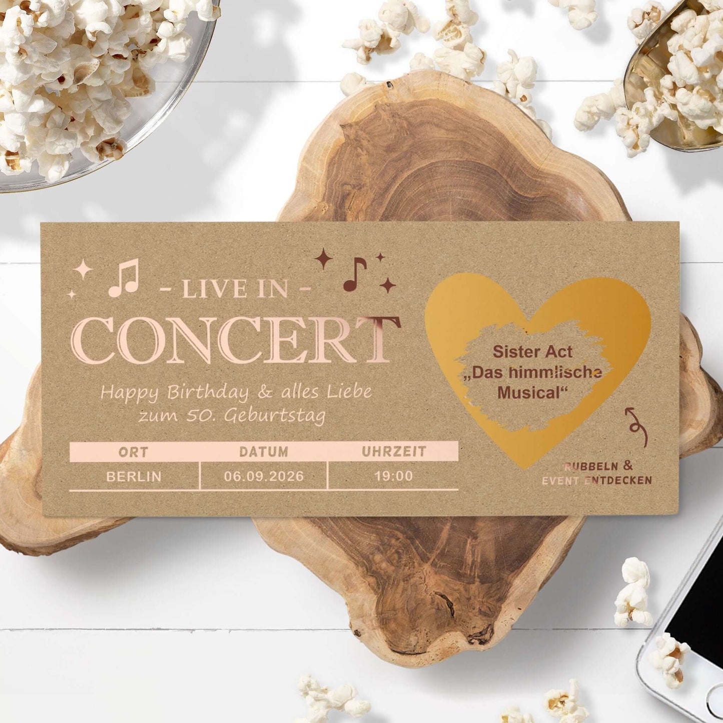 Konzert Geschenk Rubbelkarte mit personalisierten Details auf einem Holztisch, umgeben von Popcorn.