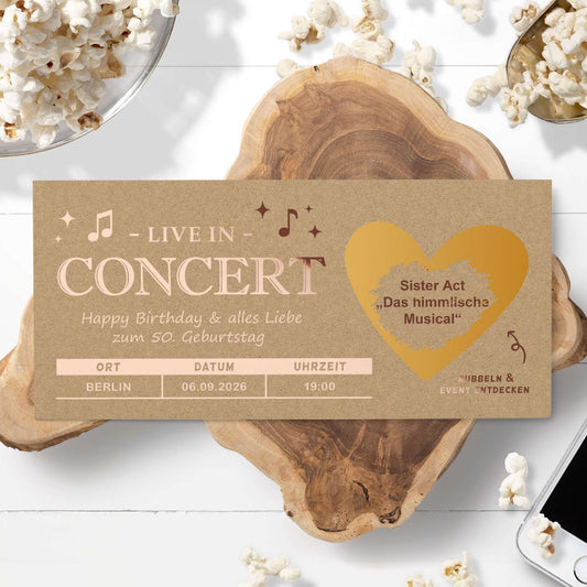 Konzert Geschenk Rubbelkarte mit personalisierten Details auf einem Holztisch, umgeben von Popcorn.