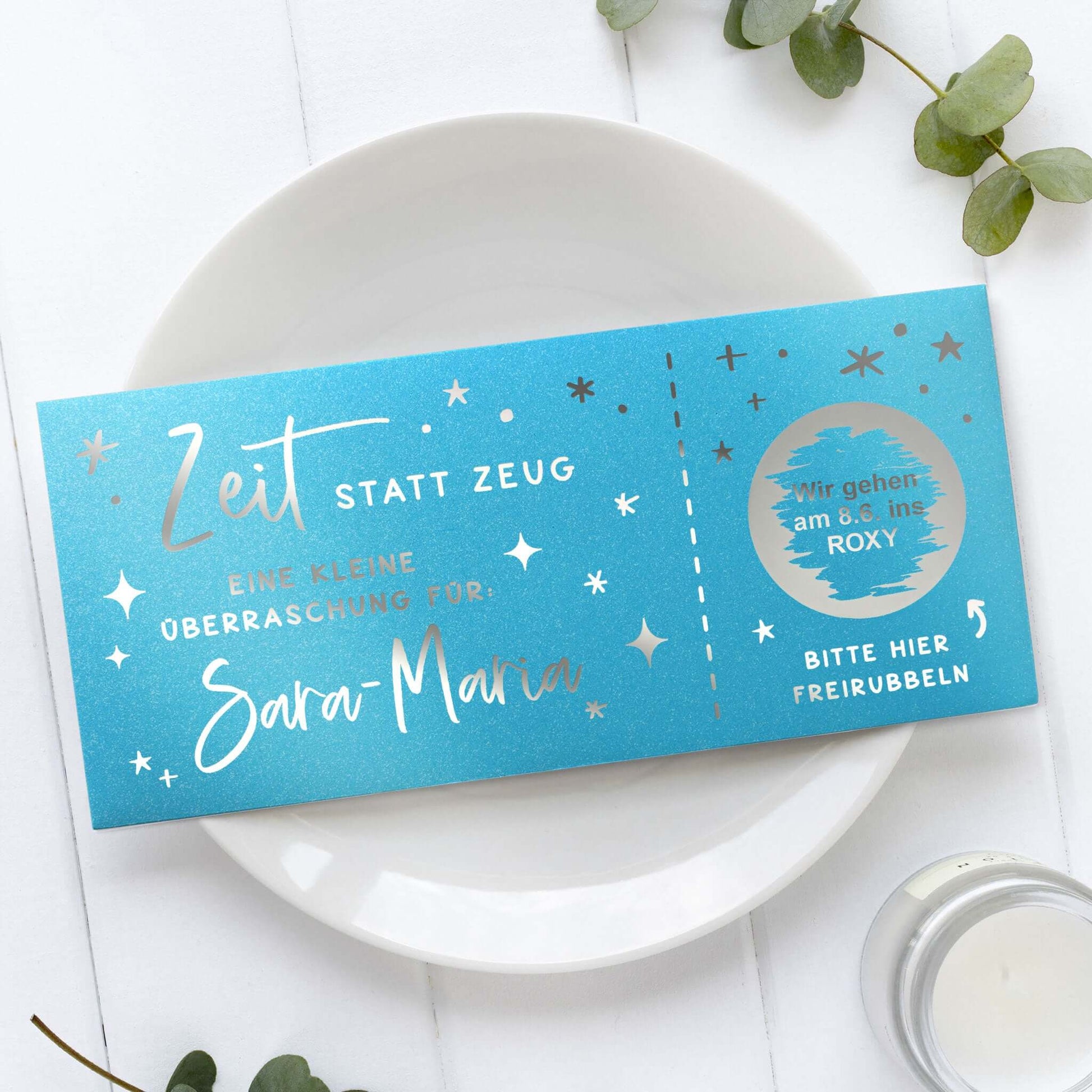 Rubbelgutschein personalisiert für Sara Maria mit dem Motto "Zeit statt Zeug" auf blauem Hintergrund.