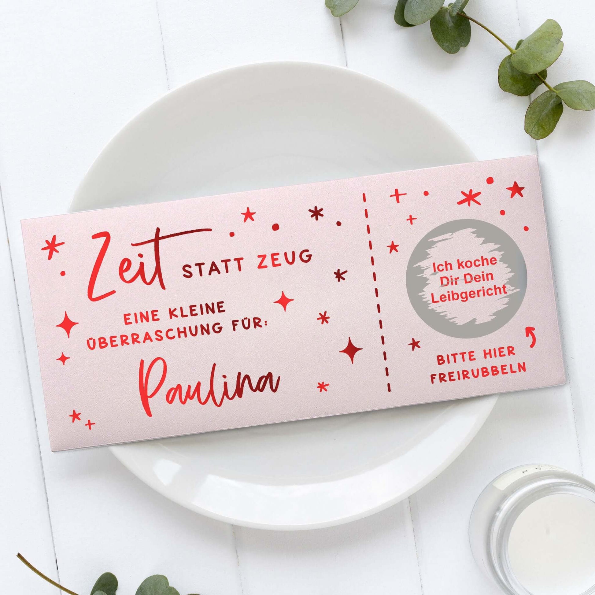 Rubbelgutschein personalisiert mit dem Text "Zeit statt Zeug" für Paulina auf einem weißen Teller.
