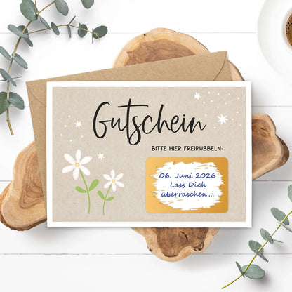 Rubbelgutschein weiße Blumen mit Umschlag und kreativen Blumenmotiven auf Holzuntergrund.