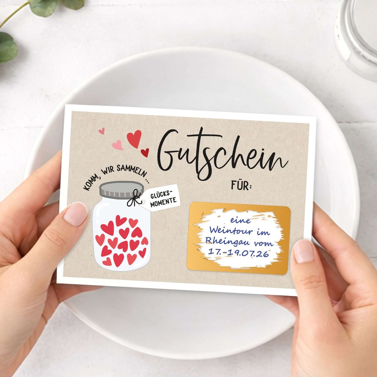 Rubbelgutschein Glücksmomente in Händen gehalten, mit dekorativem Herzen-Motiv und Gutscheininformationen.