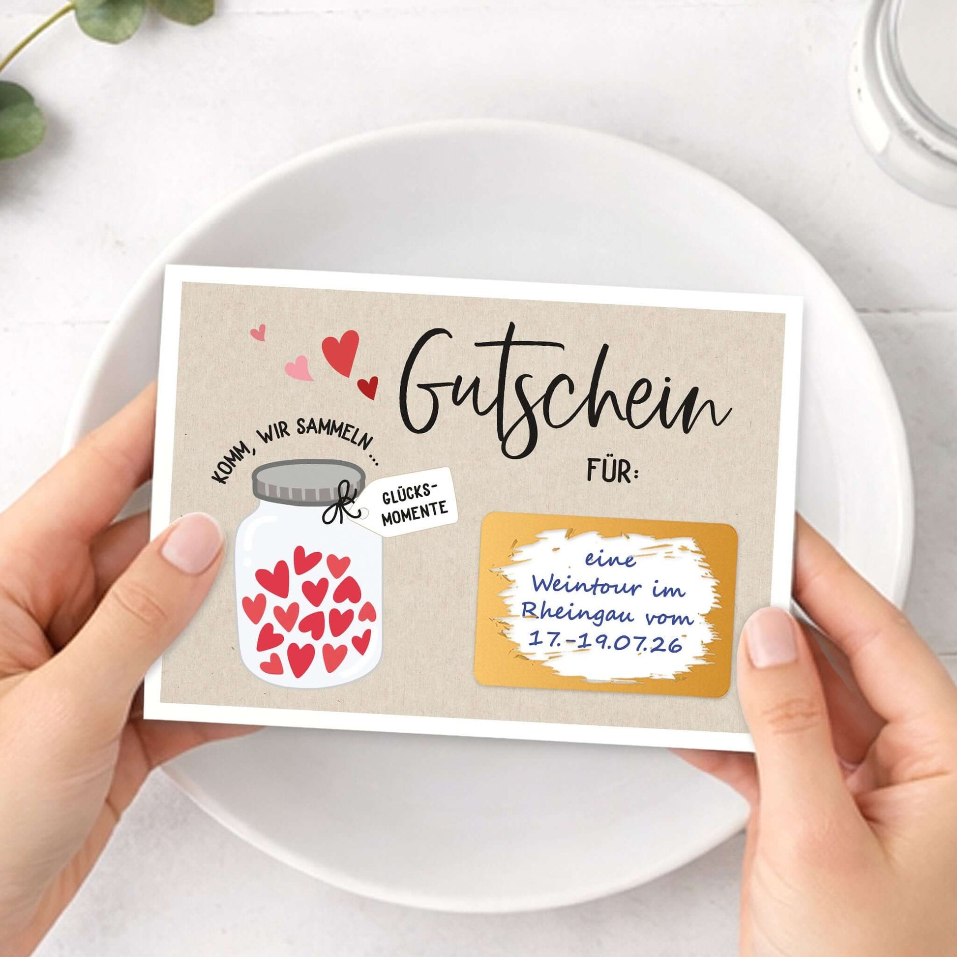 Rubbelgutschein Glücksmomente in Händen gehalten, mit dekorativem Herzen-Motiv und Gutscheininformationen.