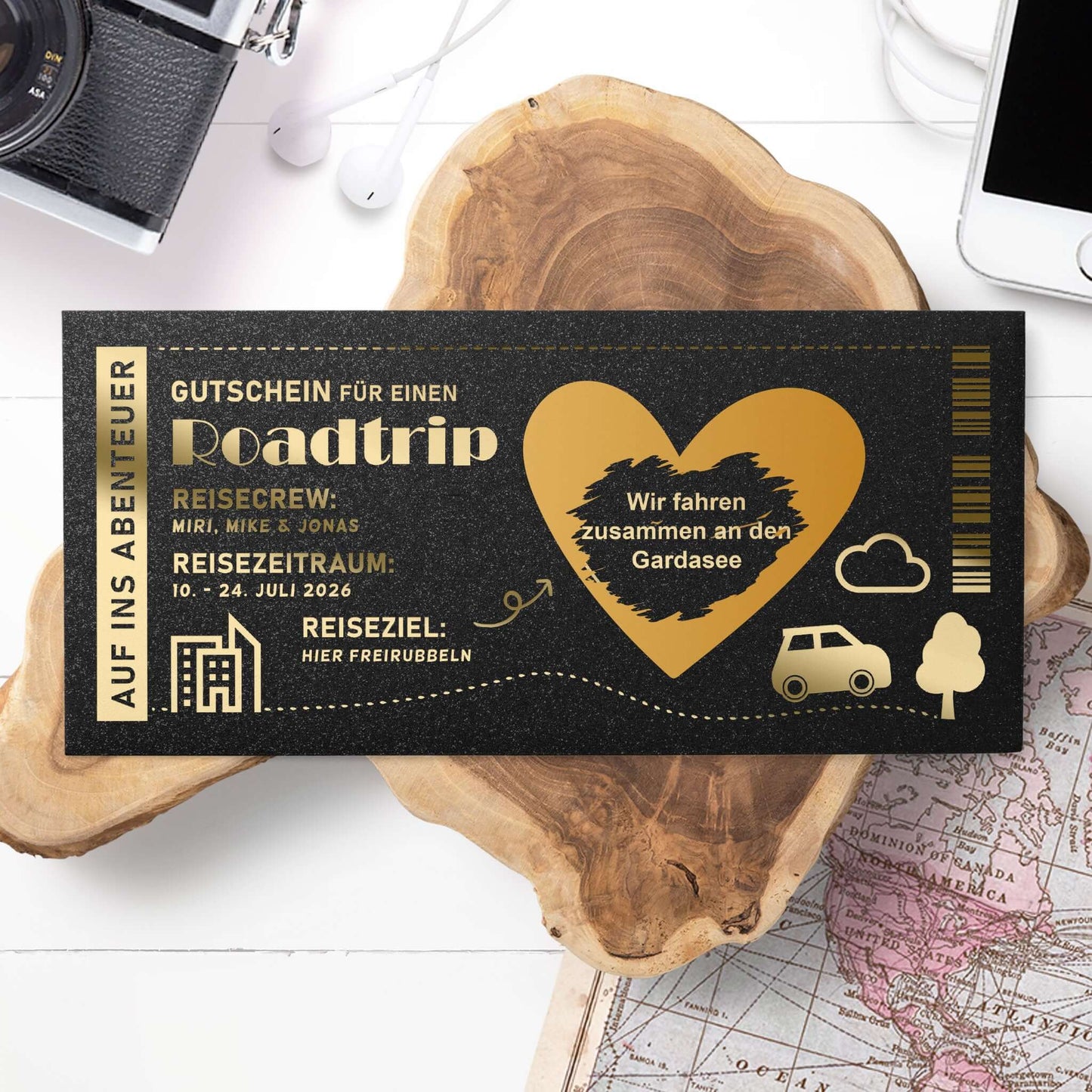 Roadtrip-Gutschein Schwarz-Gold – Lifestyle-Setting mit Reiseutensilien, Wunschtext Roadtrip an den Gardasee
