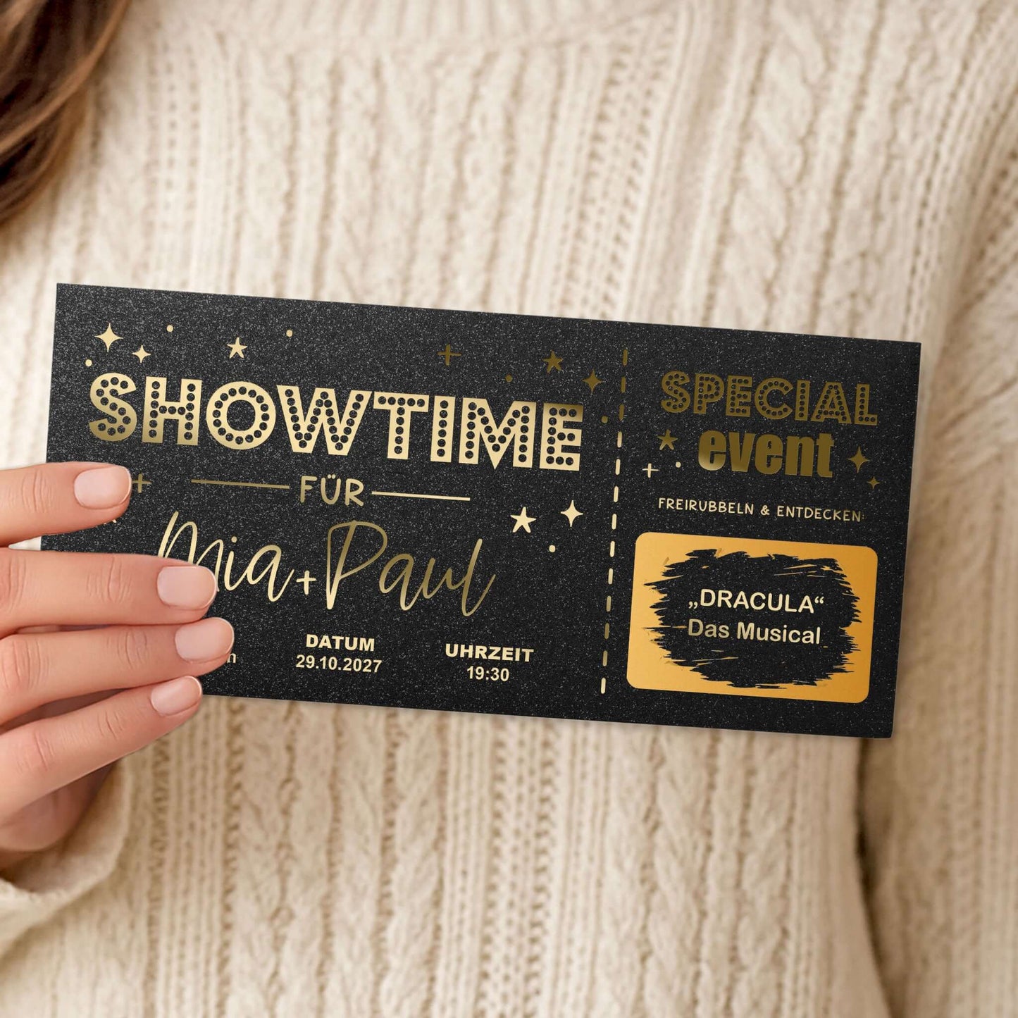 Rubbelkarte Showtime Schwarz Schimmer mit Goldfolierung, in Hand gehalten vor Pullover – Lifestyle